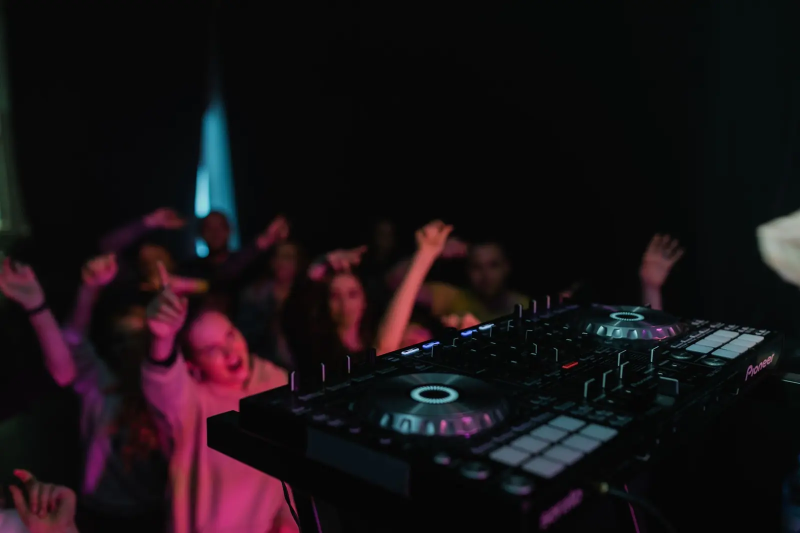 DJ booth facing an energetic dance floor under pink and blue lighting